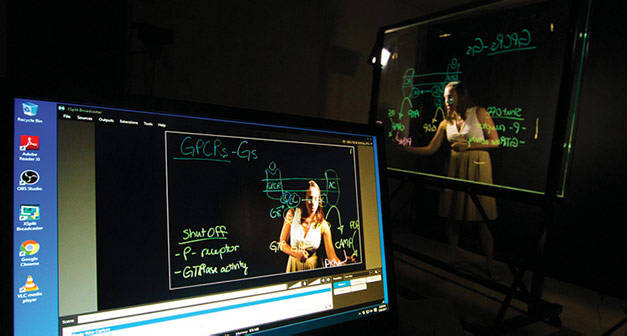 Professor Jennifer Bryant using a lightboard with her laptop in foreground.