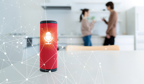 Smart speaker in foreground with man and woman facing each other in background.