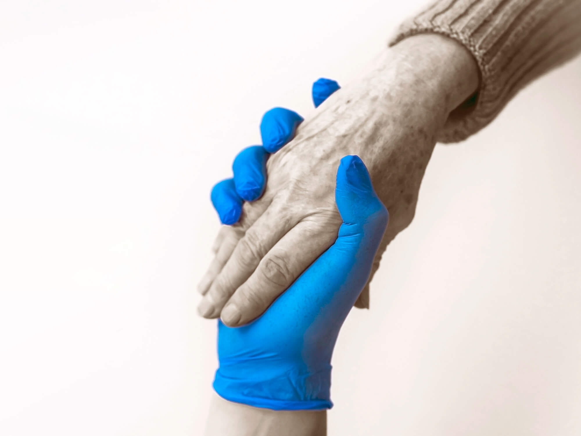 Latex gloved hand holding the hand of an elderly individual.