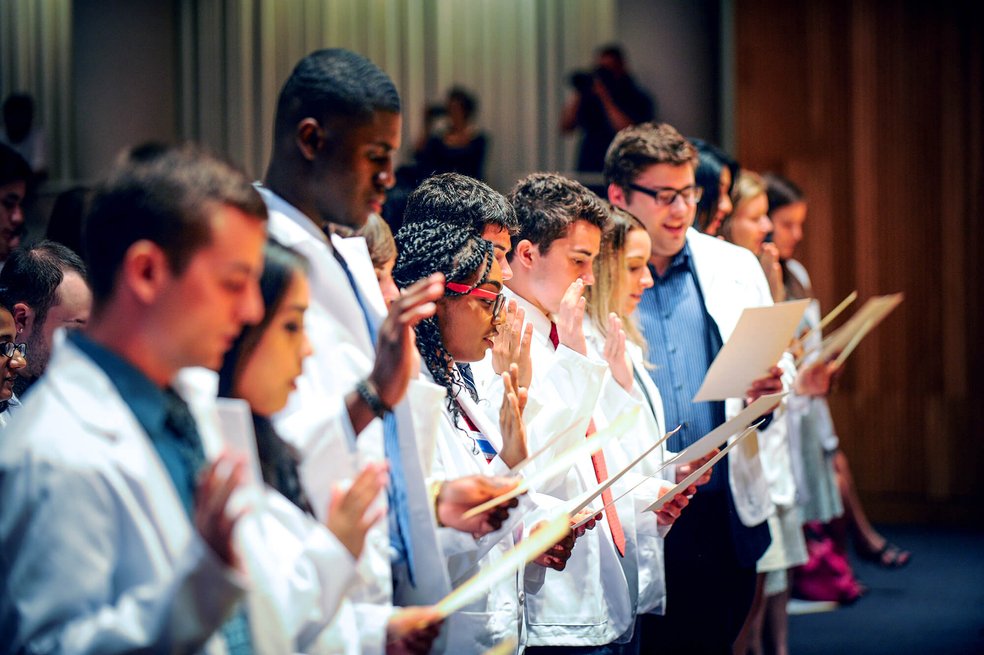 Student pharmacists in white coats reciting the Oath of a Pharmacist.