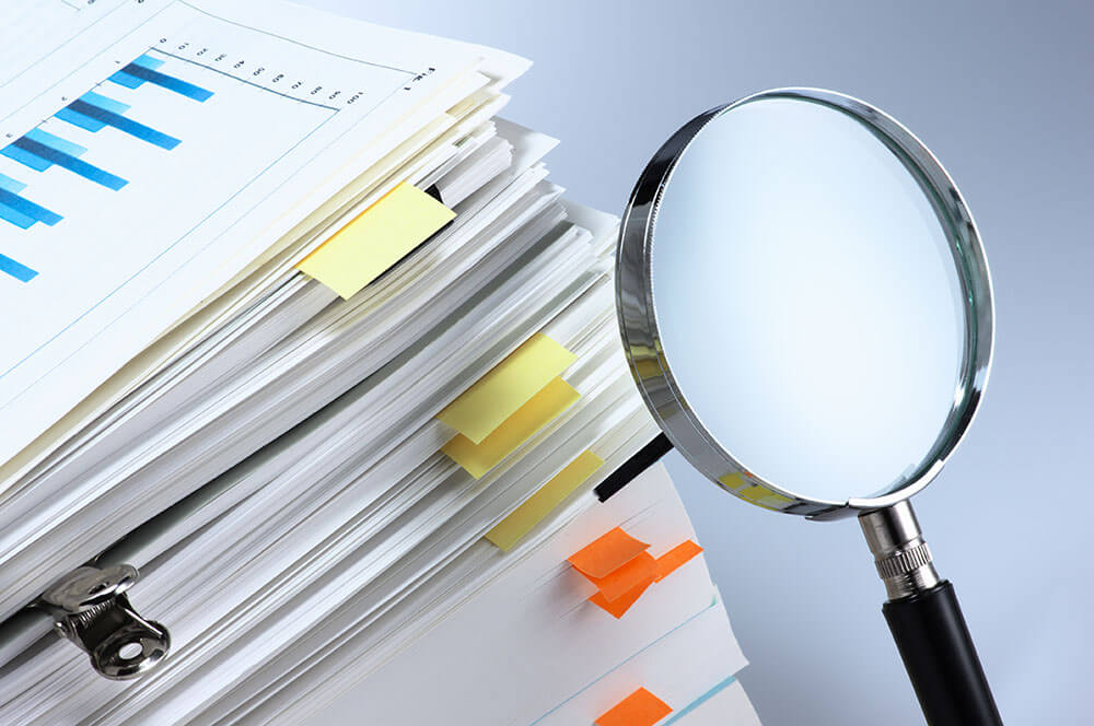 Magnifying glass pointed at large stack of papers.